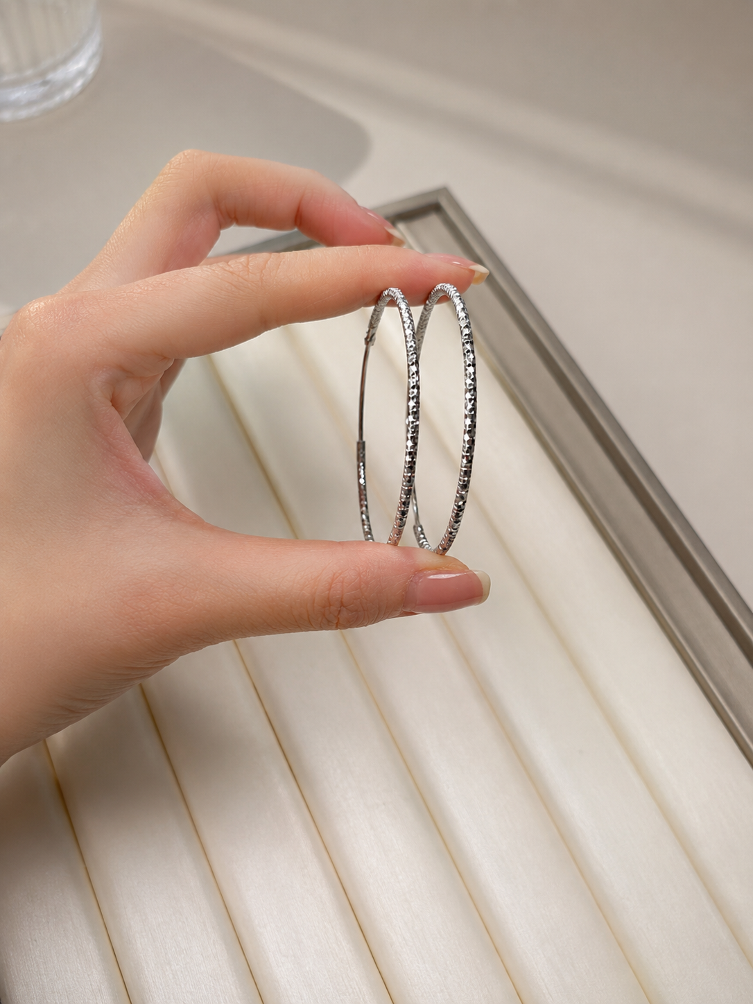 Hand holding two silver bangles on a light wooden surface