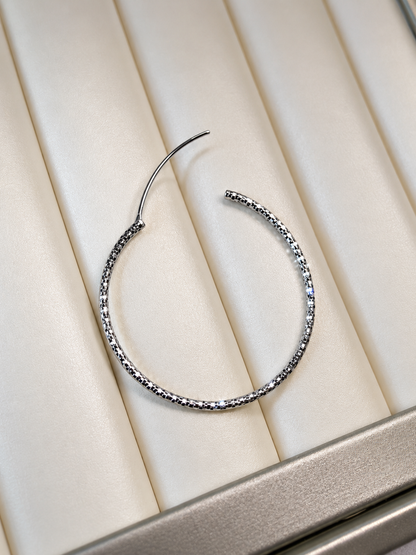 Silver hoop earring on a beige cushioned surface