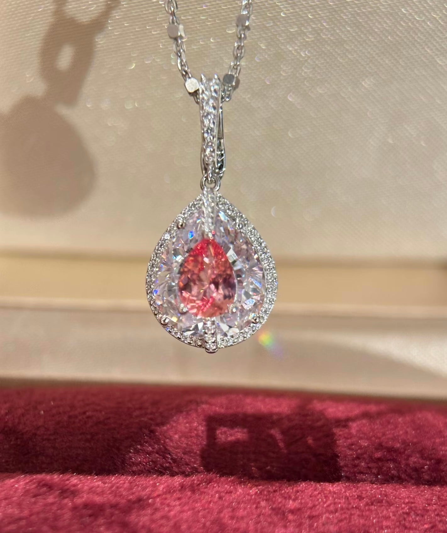 Lab-grown Padparadscha sapphire pear halo pendant necklace with silver chain from Lunelle Atelier, showcasing a vibrant orange-pink gemstone.