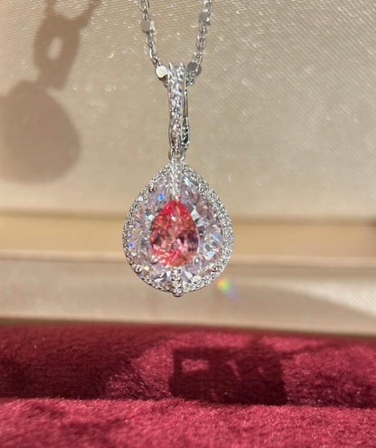 Lab-grown Padparadscha sapphire pear halo pendant necklace with silver chain from Lunelle Atelier, showcasing a vibrant orange-pink gemstone.