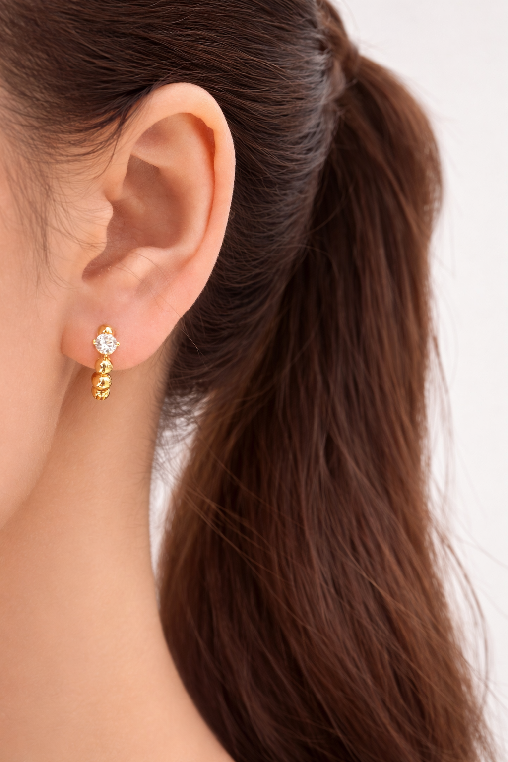 Gold earrings worn by a person with long brown hair on a white background