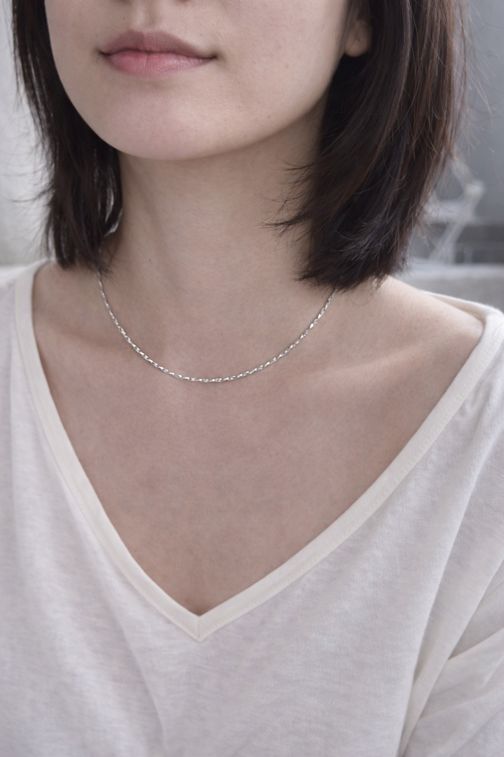 Close-up of a person wearing a delicate silver necklace against a neutral background