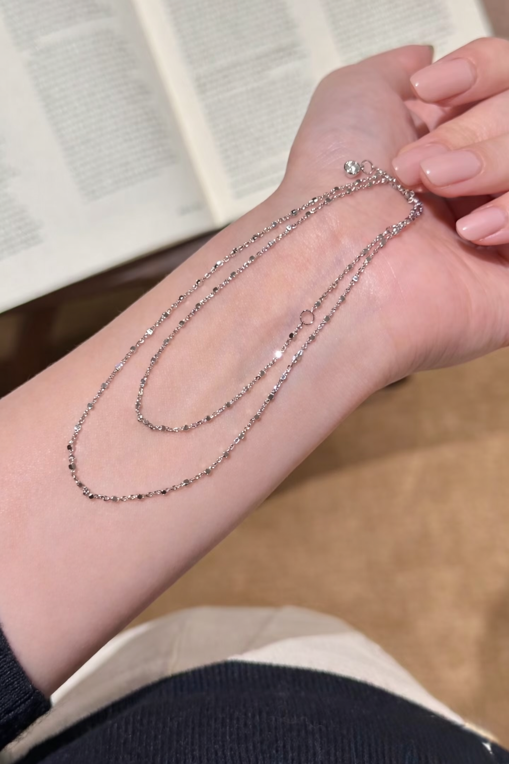 Silver chain necklace on a person's wrist with a blurred background