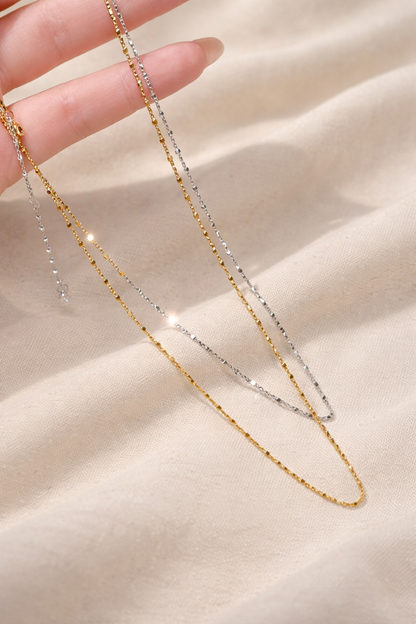 Two gold necklaces on a beige fabric background
