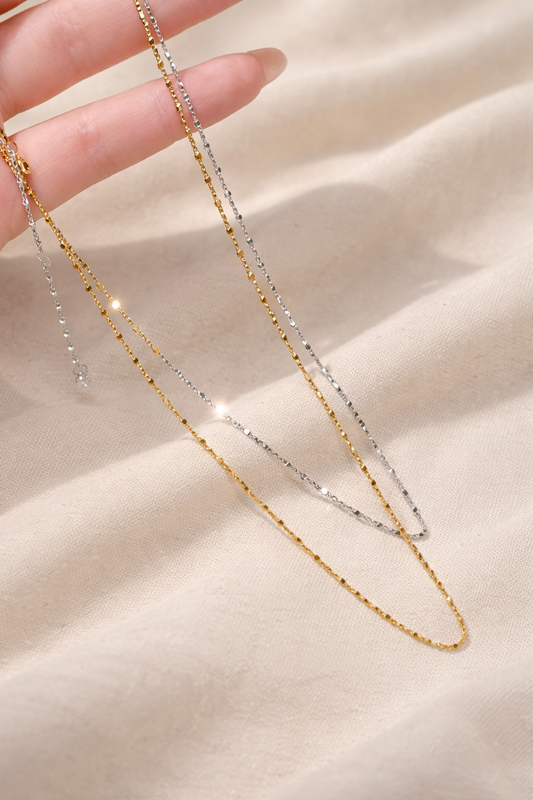 Two gold necklaces on a beige fabric background