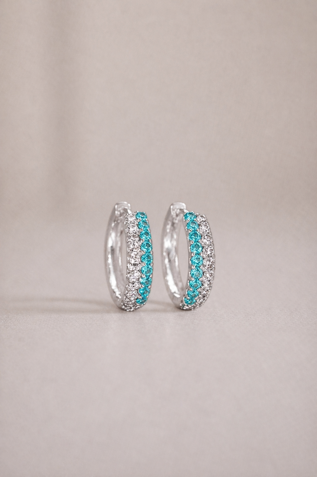 Silver hoop earrings with turquoise stones on a beige background