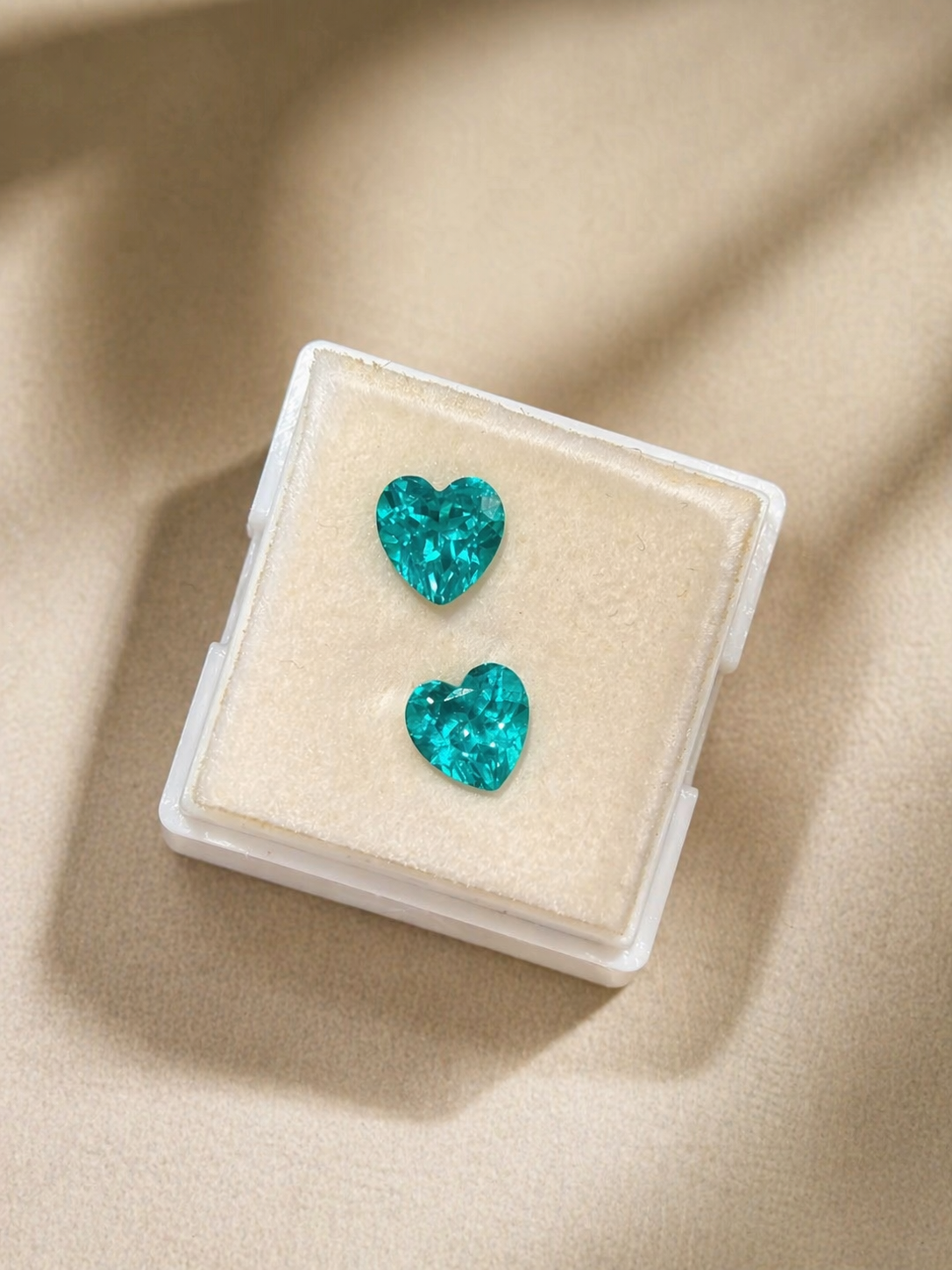 Turquoise heart-shaped earrings in a clear jewelry box on a beige fabric background