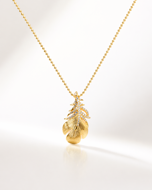 Gold necklace with a leaf-shaped pendant on a white background