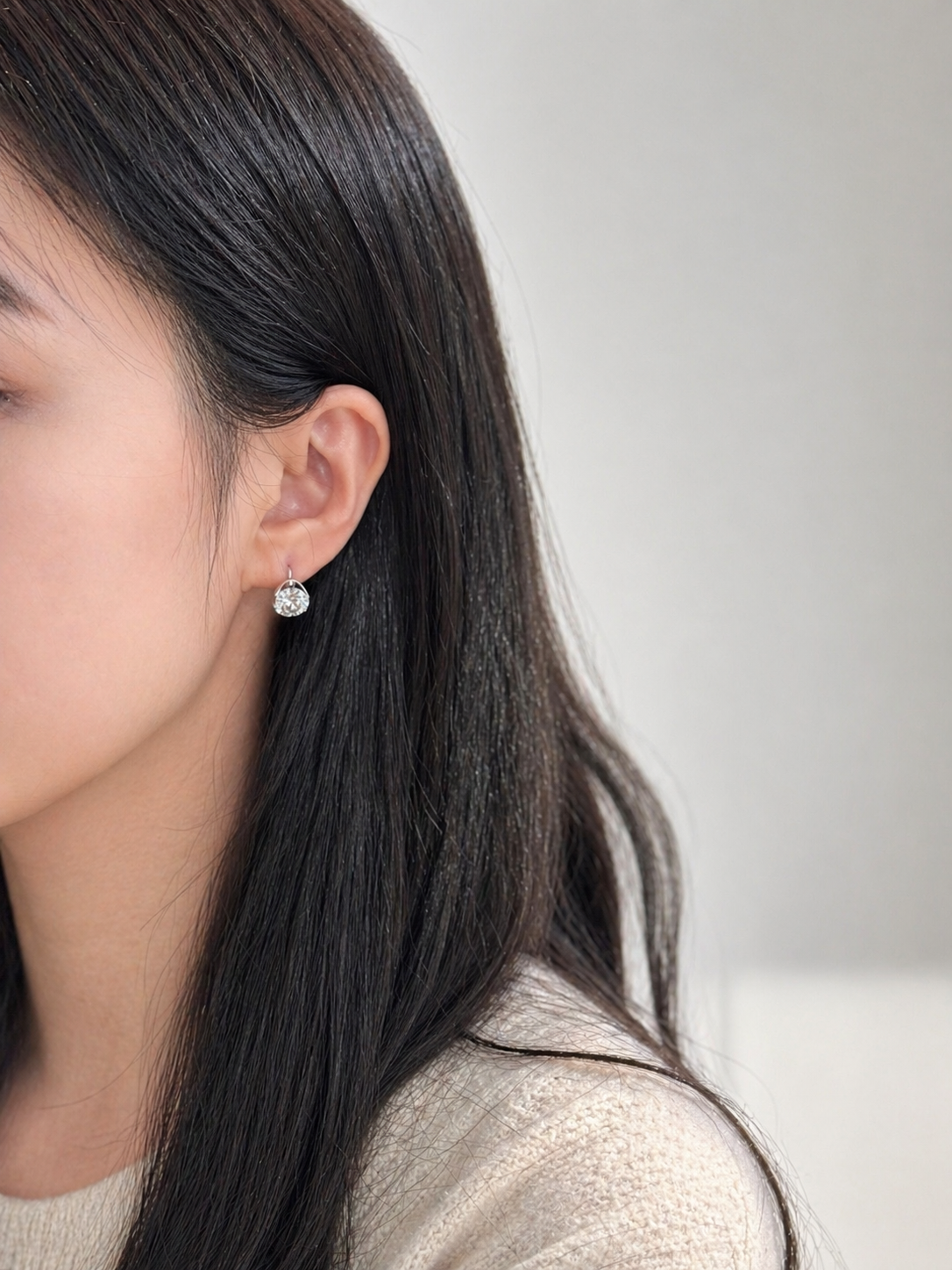Close-up of a person wearing a diamond earring with a neutral background