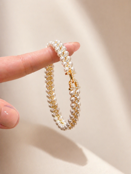 Pearl and gold bracelet held by a hand against a white background
