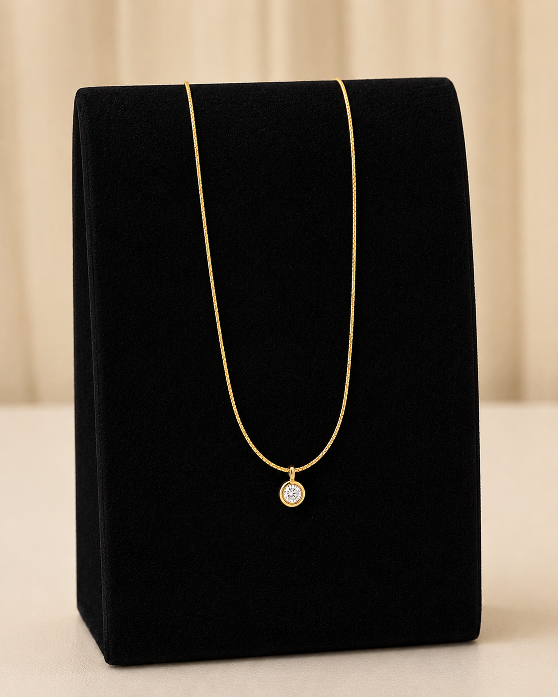 Gold necklace with a diamond pendant on a black velvet stand against a beige background
