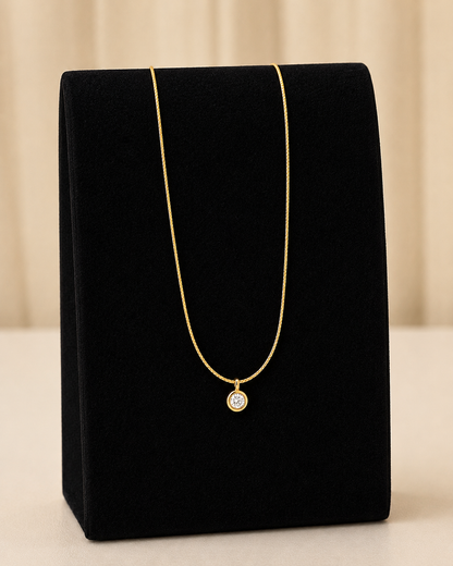 Gold necklace with a diamond pendant on a black velvet stand against a beige background