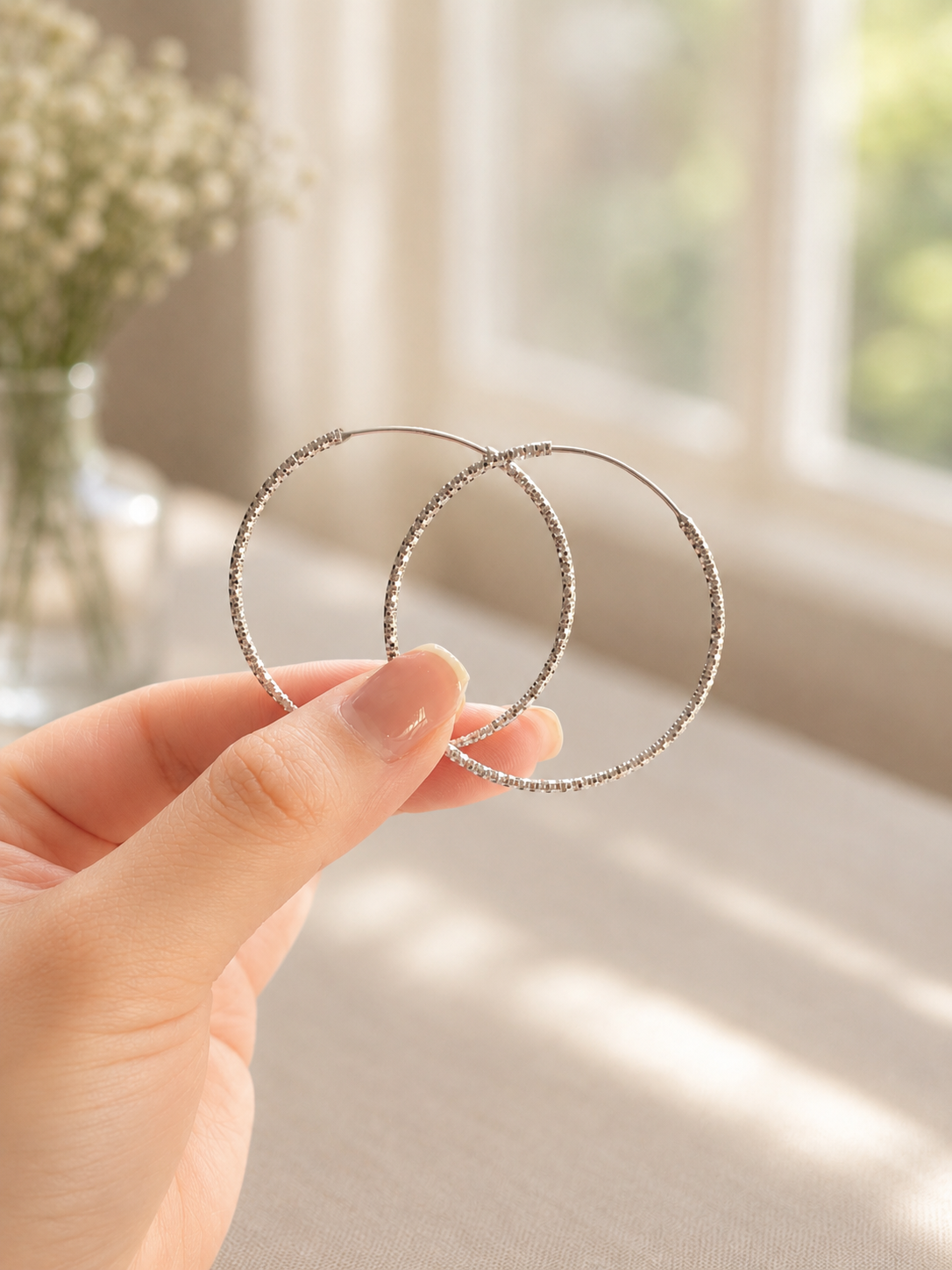Hand holding two silver hoop earrings with a blurred indoor background