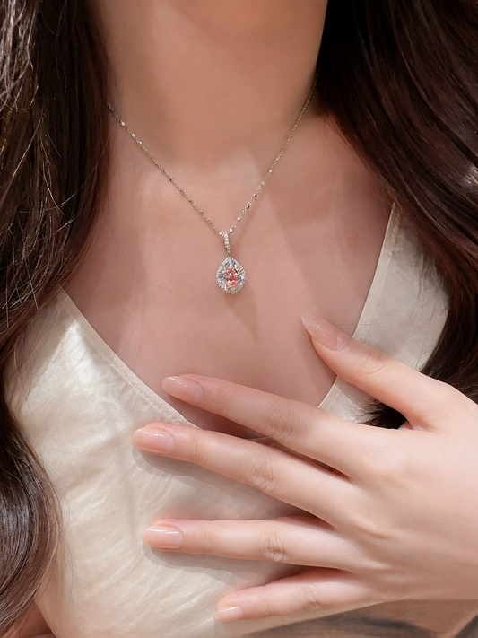 Lab-grown Padparadscha sapphire pear-shaped halo pendant necklace by Lunelle Atelier, featuring a vibrant orange-pink gemstone.