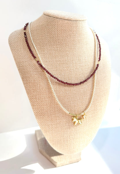 Necklace with purple beads and a gold butterfly pendant on a beige jewelry display.
