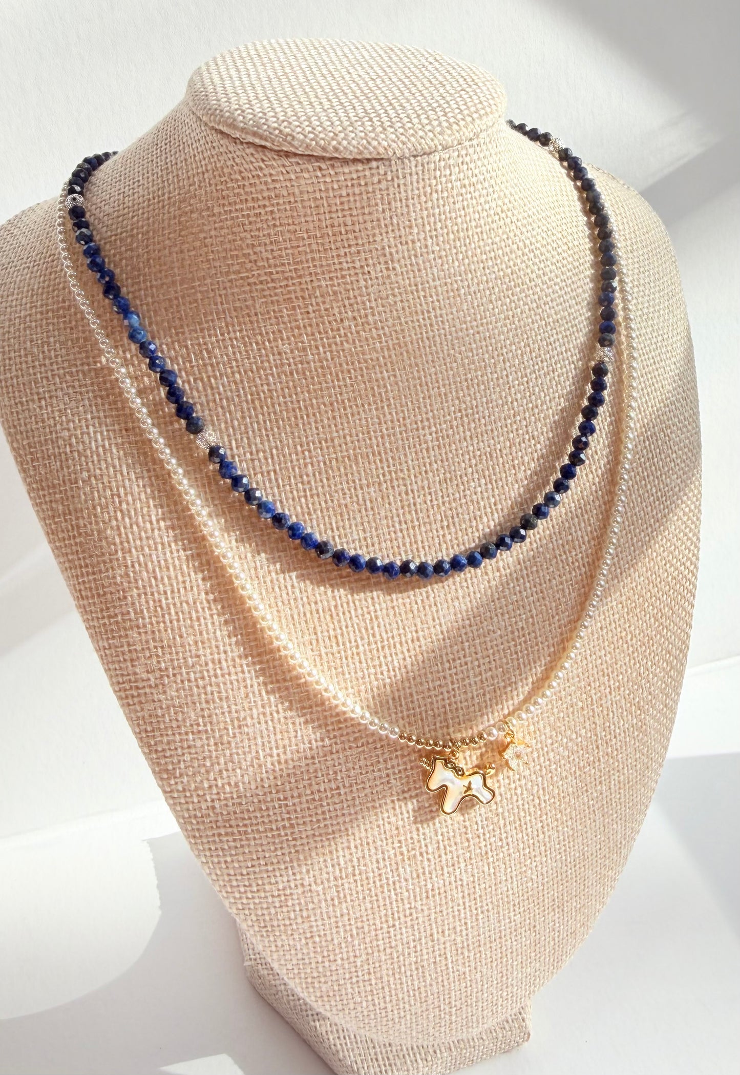 Necklace with blue beads and a gold pendant on a beige mannequin bust.