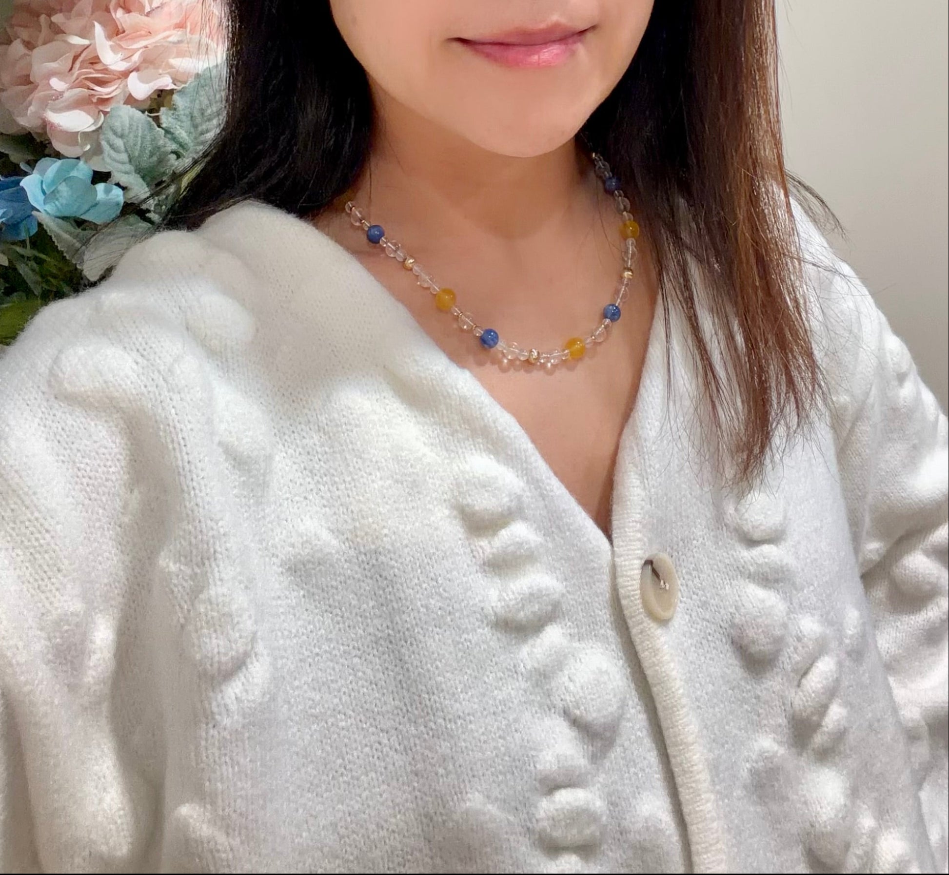 Woman wearing a white sweater in a room with a blue and yellow gemstone necklace.