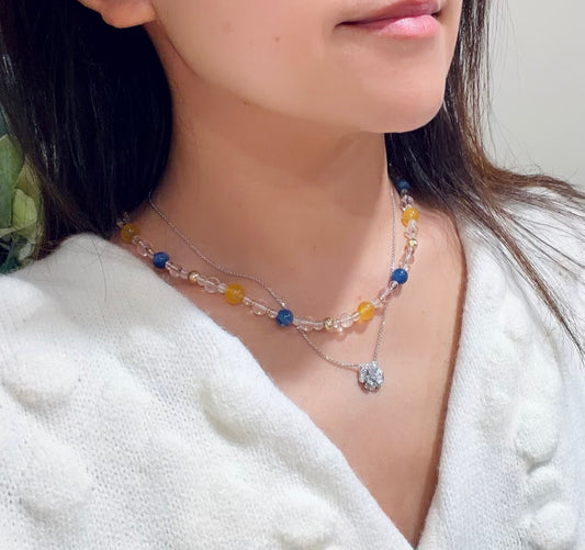 Close-up of a person wearing a blue and yellow beaded necklace with a white sweater.