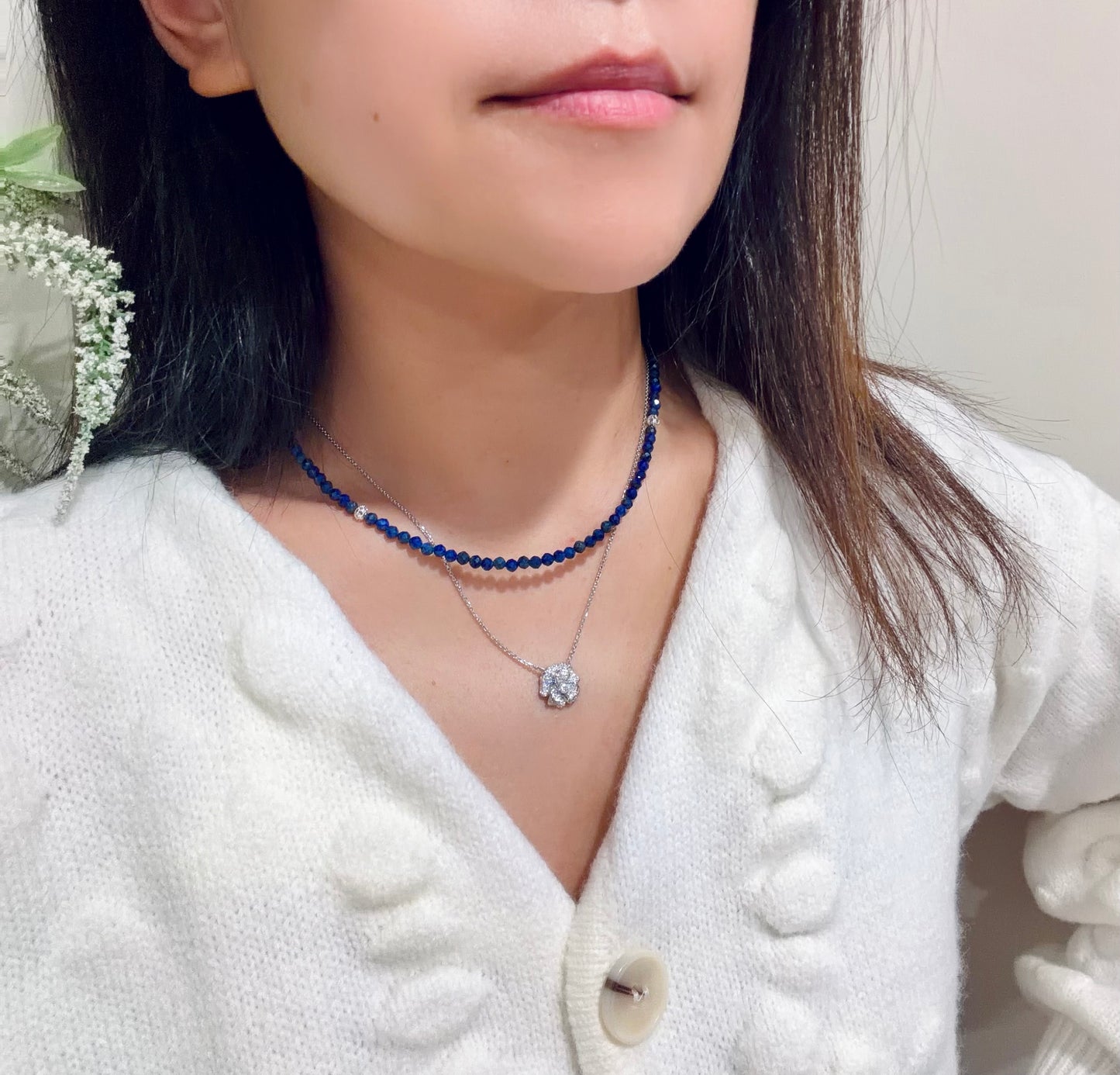 Person wearing a blue beaded necklace with a white cardigan