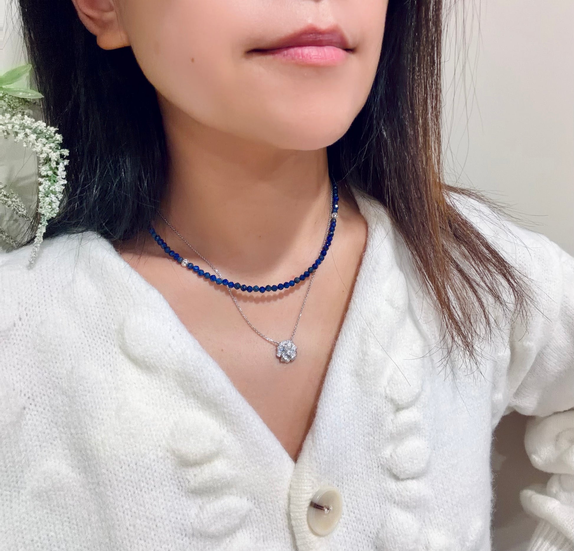 Person wearing a blue beaded necklace with a white cardigan