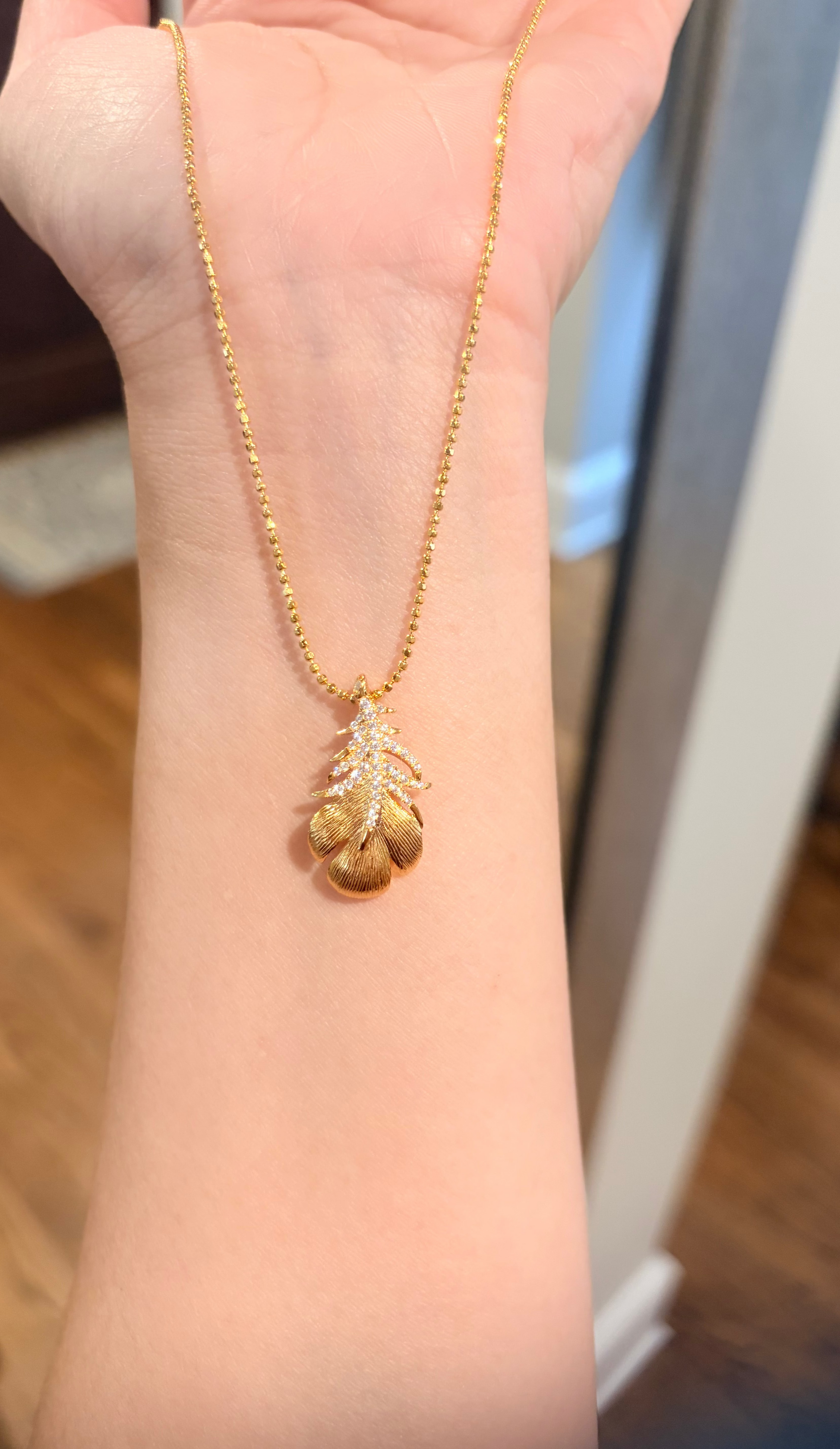 Gold necklace with a pendant on a person's wrist.