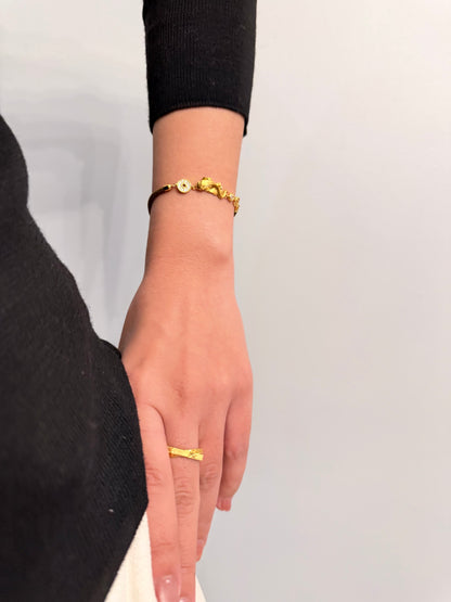 Gold bracelet and ring on a person's wrist against a neutral background
