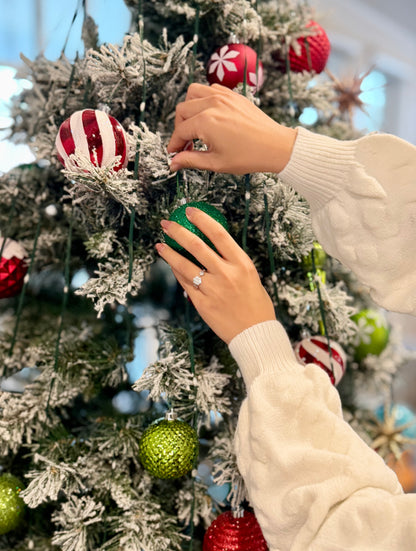 Person decorating a Christmas tree with colorful ornaments showing the silver ring with Moissanite Gemstone