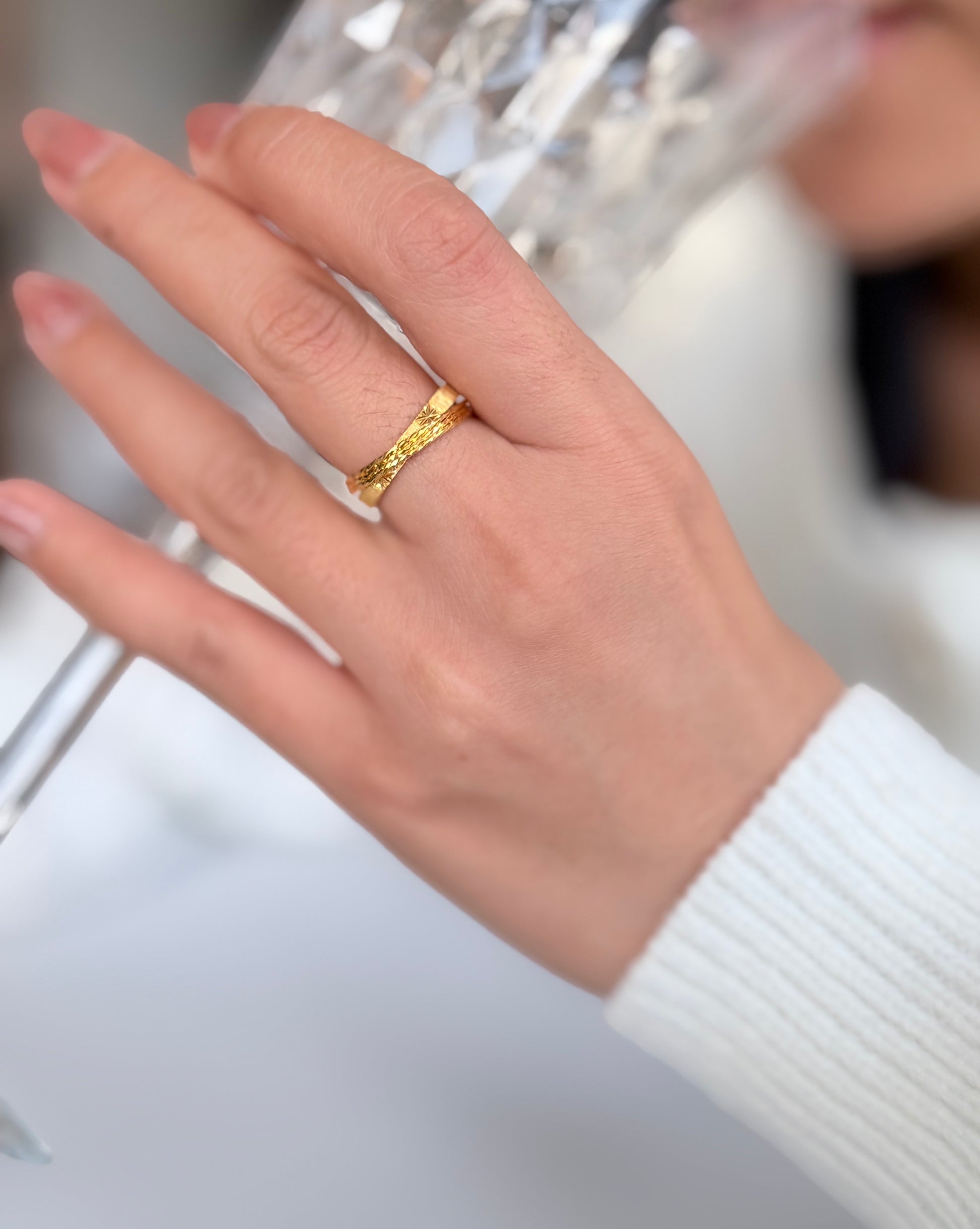 Hand wearing a gold ring with a blurred background