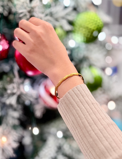 Hand wearing a gold color bracelet in front of a decorated Christmas tree.