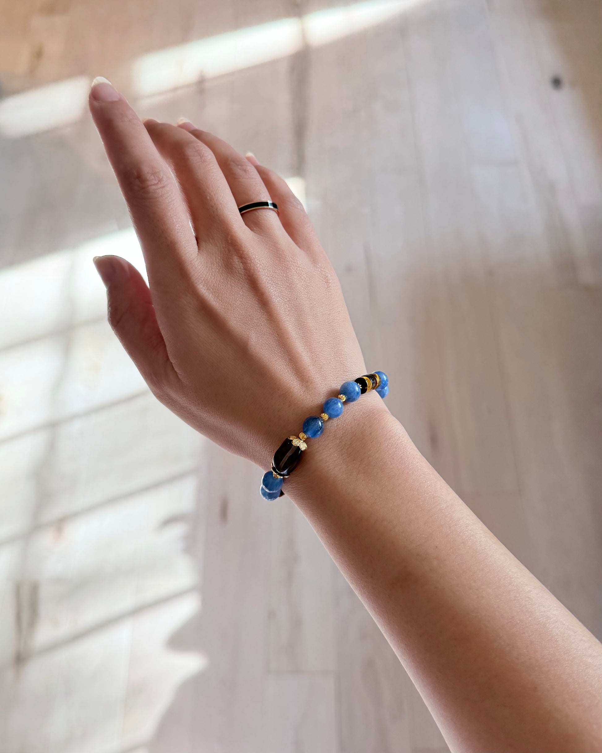 Hand wearing a blue beaded bracelet with a blurred background