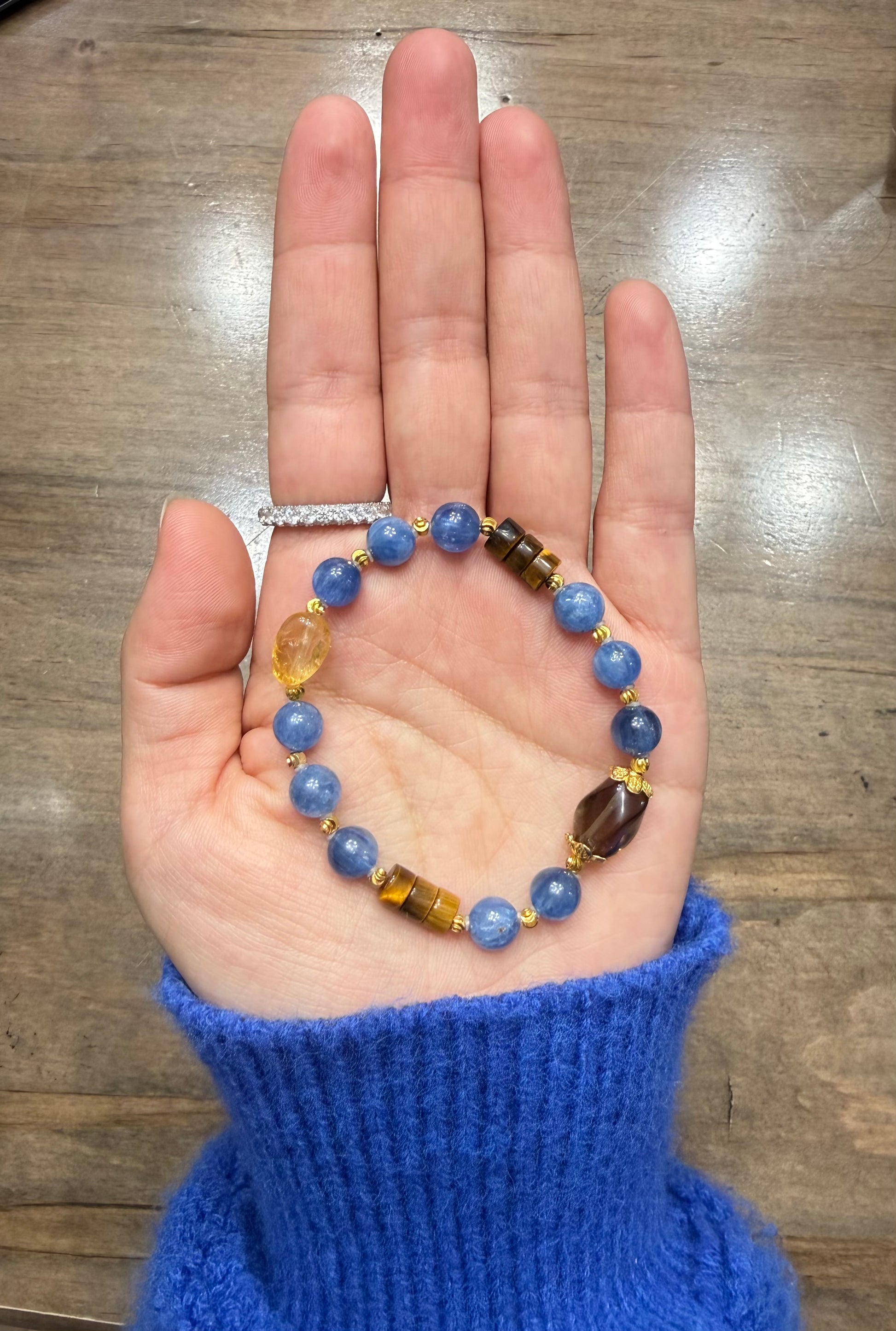 Hand holding a blue beaded bracelet on a wooden surface