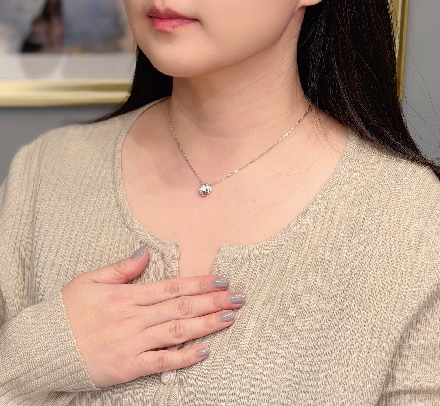 Person wearing a necklace with a small round pendant, hand resting on chest.