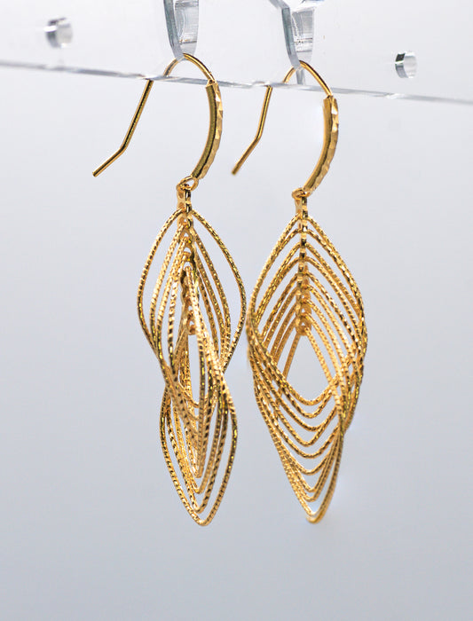 Gold leaf-shaped earrings on a clear stand against a white background