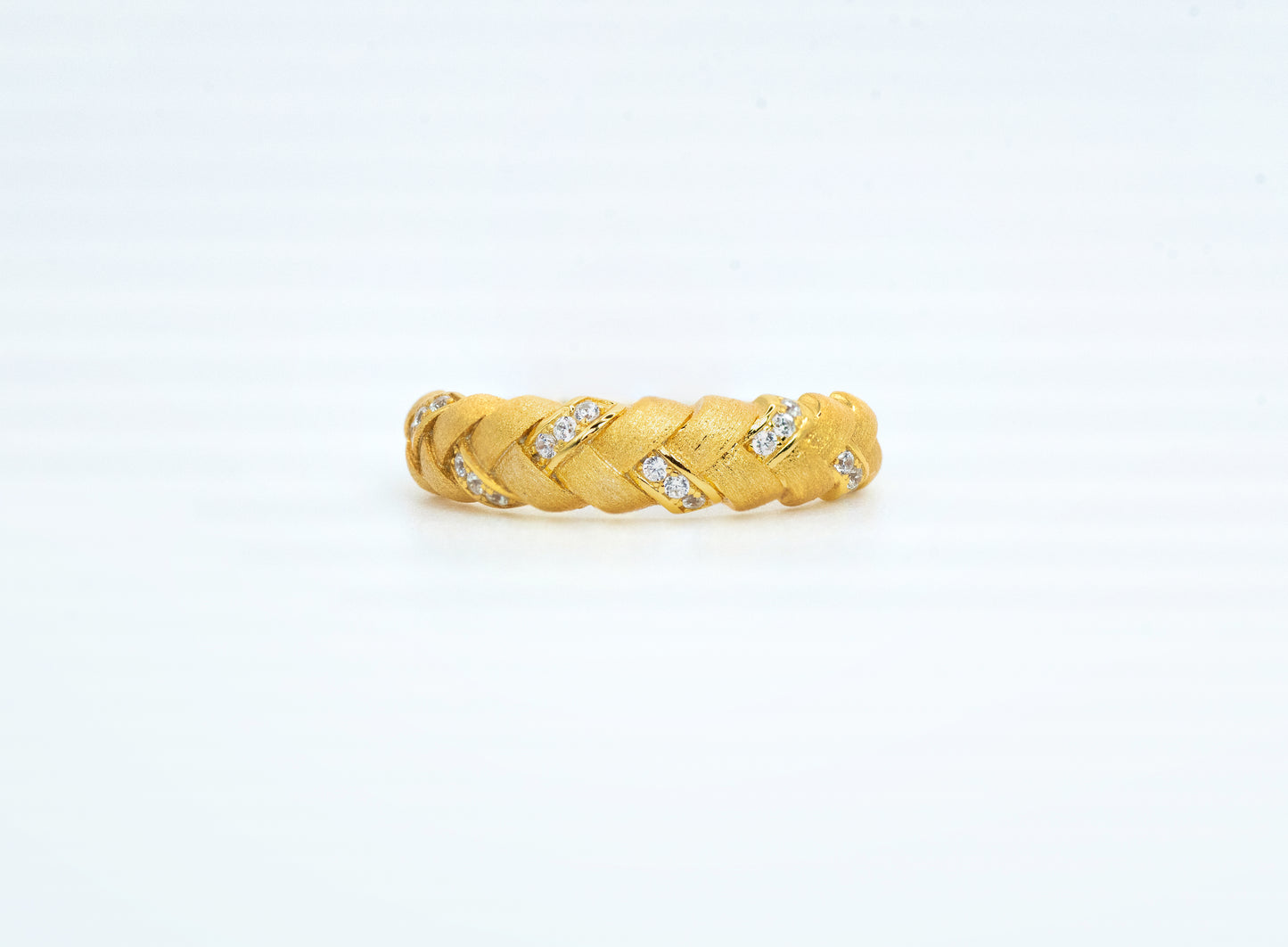 Gold braided ring with embedded diamonds on a light gray background