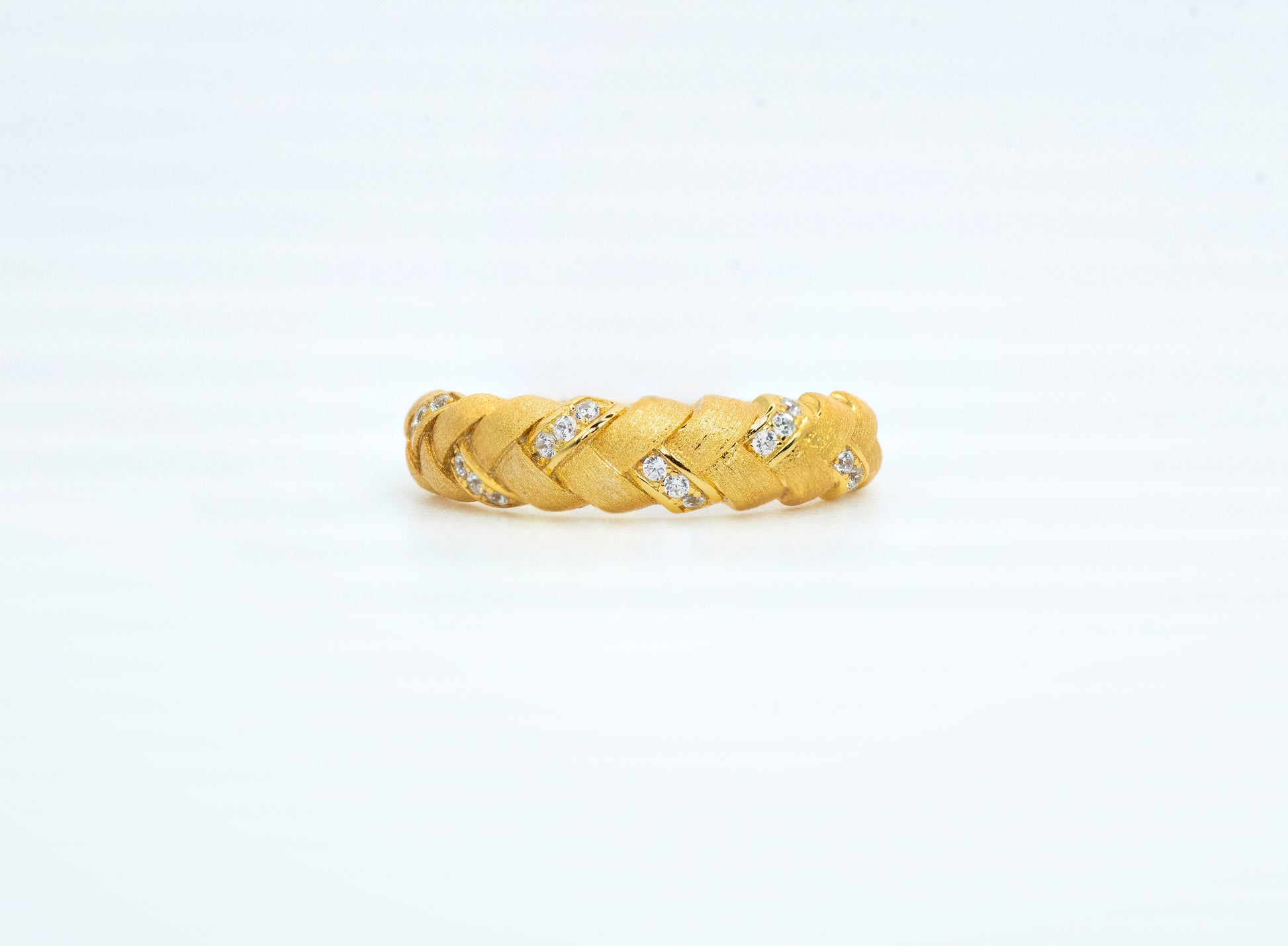 Gold braided ring with embedded diamonds on a light gray background
